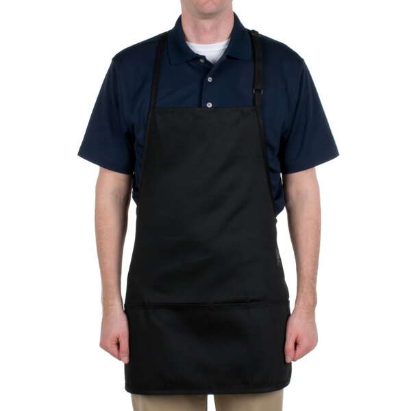 A man wearing a black Chef Revival bib apron with 3 pockets in a professional kitchen.