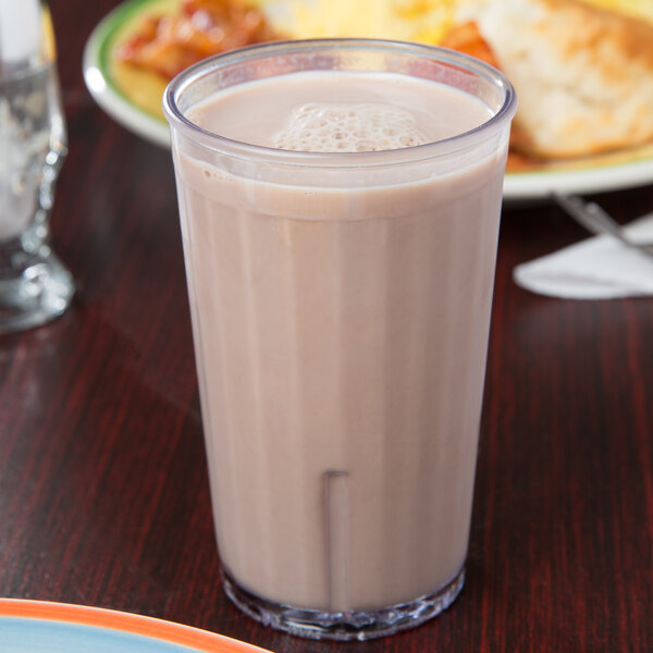 A clear GET SAN plastic tumbler filled with chocolate milk on a table.