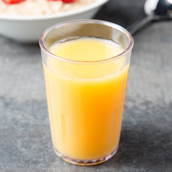 A clear plastic tumbler filled with orange juice next to a bowl of cereal.