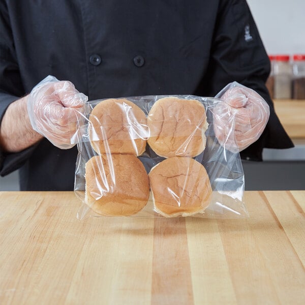 A person in a chef's uniform holding a LK Packaging plastic bag of hamburger buns.
