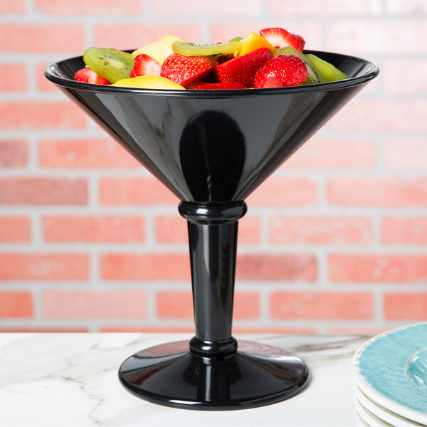 A black plastic martini glass filled with fruit on a table.