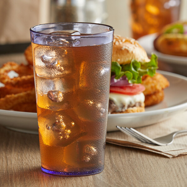 A blue plastic tumbler filled with ice tea on a table with a burger on a plate.