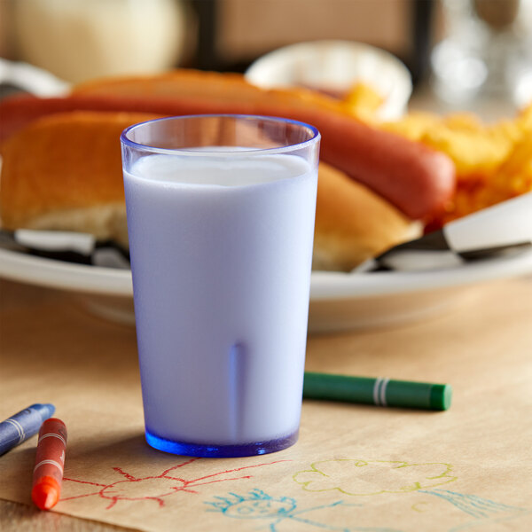 A blue SAN plastic tumbler filled with milk on a table.