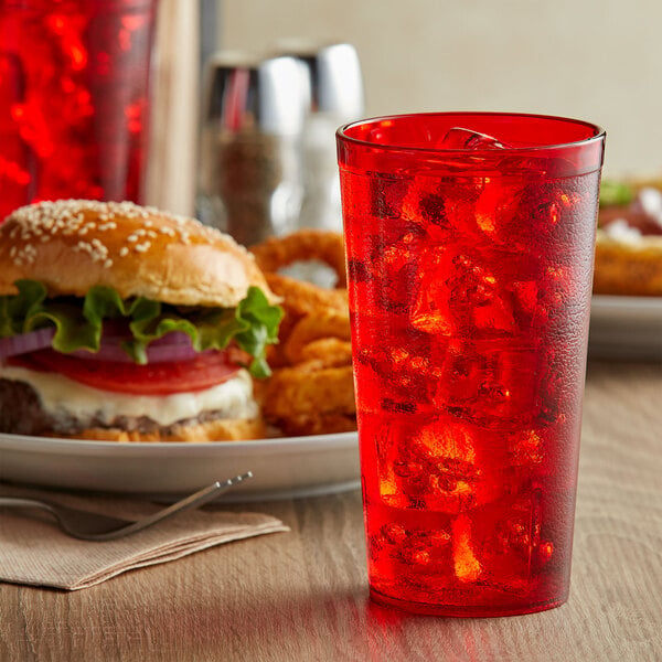 A close up of a red GET plastic tumbler filled with red soda on a table with a burger and fries.
