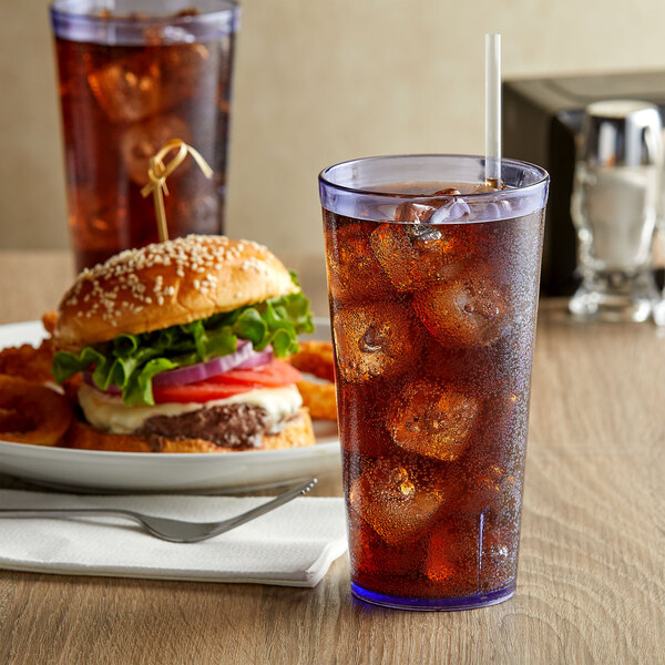 A blue plastic tumbler filled with ice tea on a table with a plate of food.
