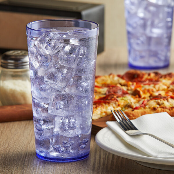 A blue SAN plastic tall tumbler filled with ice water on a table with a pizza.