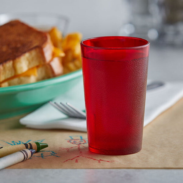 A red GET plastic tumbler filled with a red drink on a table next to crayons.