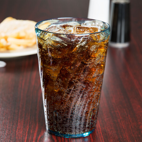A GET Tahiti jade plastic tumbler filled with soda and ice on a table with a plate of fries.