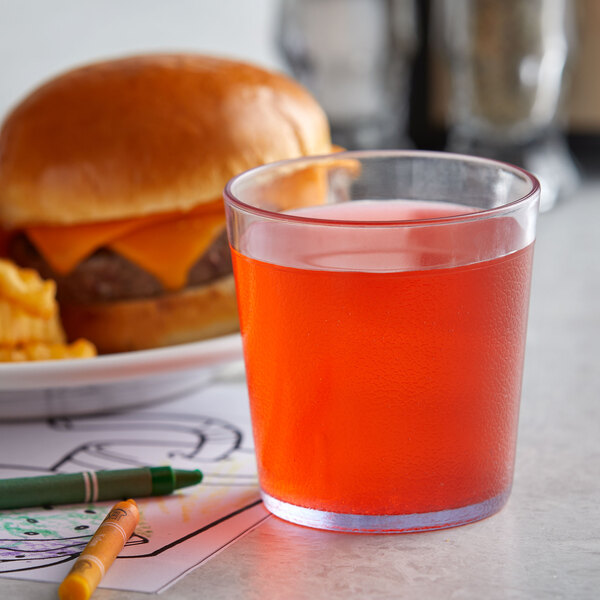 A clear customizable plastic tumbler filled with orange liquid on a table next to a hamburger and crayons.