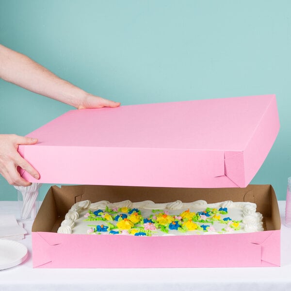 A person opening a pink Baker's Mark full sheet cake box with a cake inside.