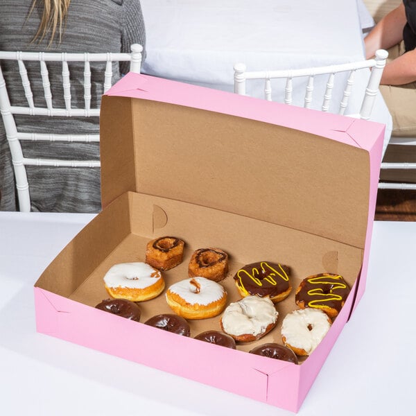A Baker's Mark pink bakery box of donuts on a table at a catering event.