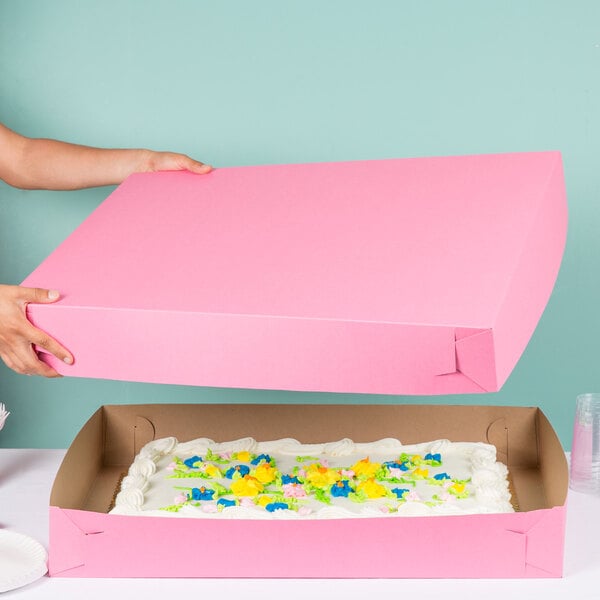 A person holding a pink Full Sheet Cake box with a cake inside.