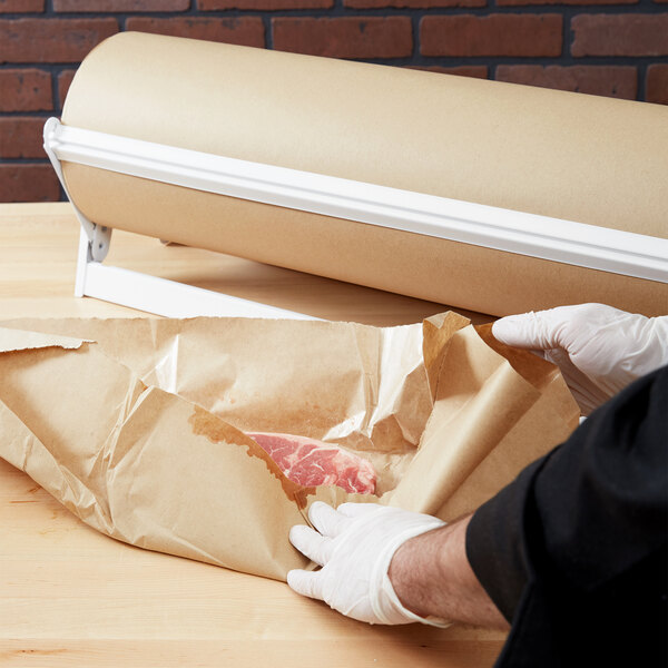 A person wearing gloves uses Bagcraft Packaging EcoCraft Freezer Paper to pack meat.