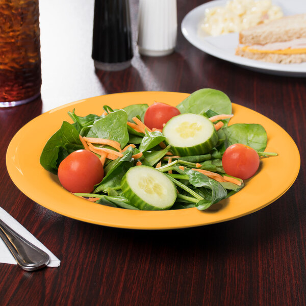 A plate of salad with cucumbers, tomatoes, and carrots in a yellow melamine bowl.