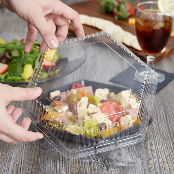 A hand holding a Genpak Smart-Set clear plastic container with food in it.