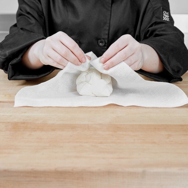 A woman's hands in a school kitchen using San Jamar Grade 40 bleached cheesecloth to wrap a piece of food.