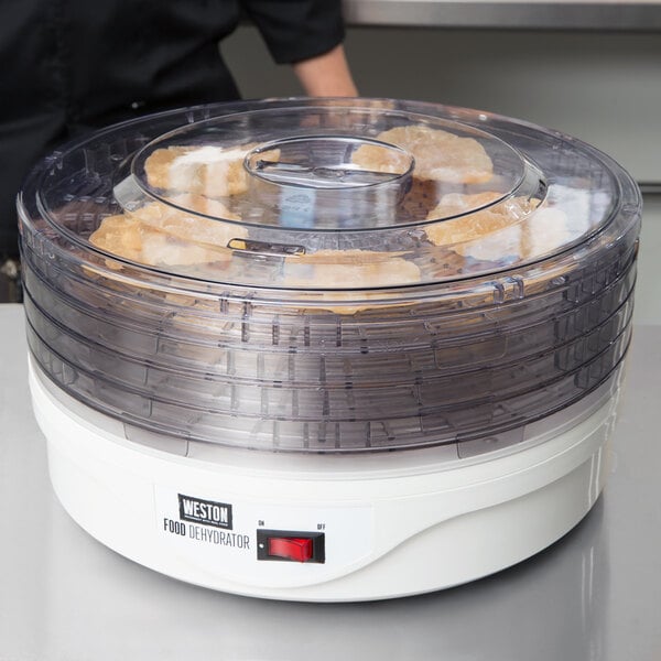 A Weston 4-tier food dehydrator on a counter with clear containers of food inside.