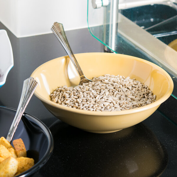 A Tablecraft melamine bowl filled with sunflower seeds on a hotel buffet counter with a spoon.