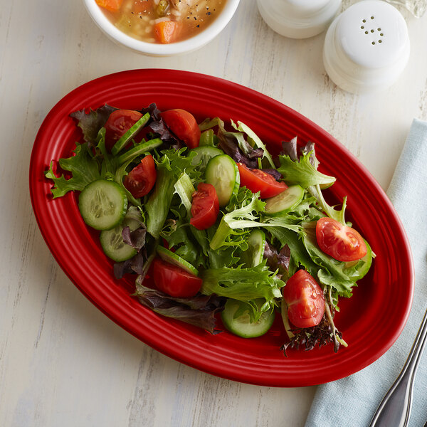 A white Tuxton oval china platter with salad, tomatoes, cucumbers, and lettuce on it.