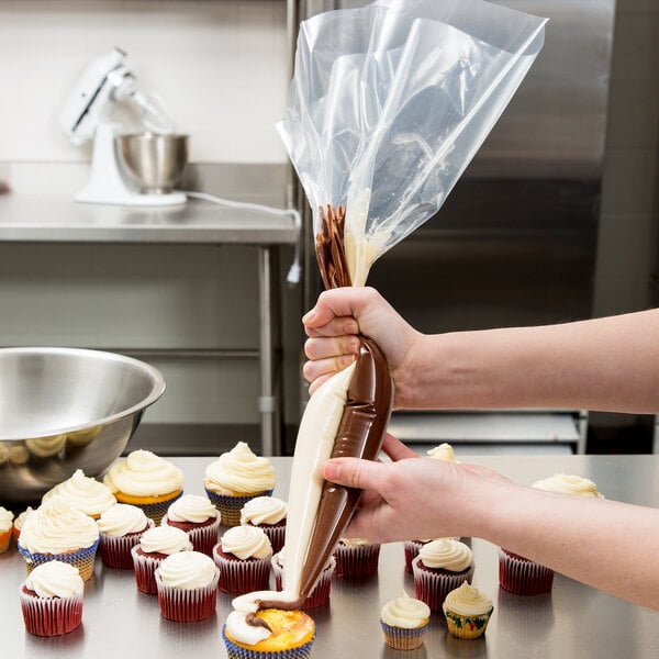 A person using an Ateco clear plastic pastry bag with white frosting to decorate a cupcake.