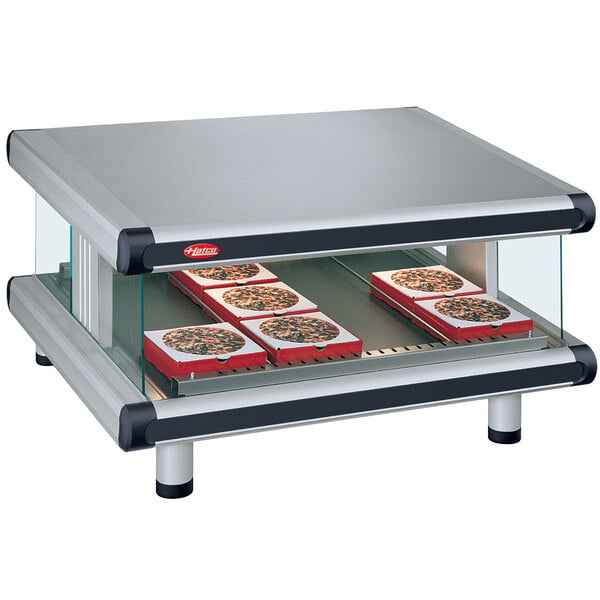 A Hatco countertop food warmer with a slanted shelf holding trays of pizzas.