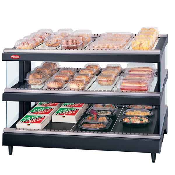 A Hatco slanted double shelf heated glass merchandising warmer on a countertop with food in it.