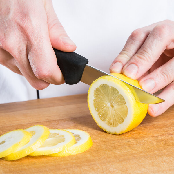 A person using a Victorinox boning knife with a black Fibrox handle to cut a lemon.