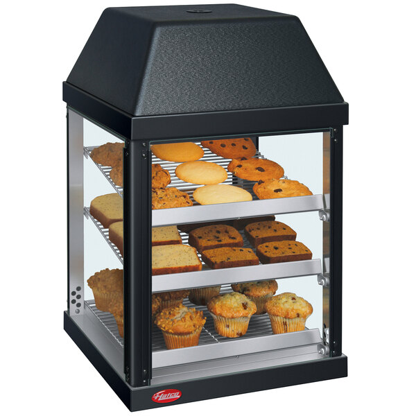 A Hatco countertop display warmer with muffins and cookies on shelves.