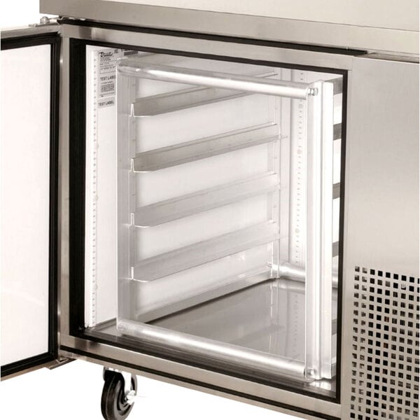 A stainless steel True half height sheet pan rack in a refrigerator with open doors.