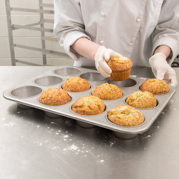 A person in a white coat putting a muffin in a Chicago Metallic jumbo muffin pan.