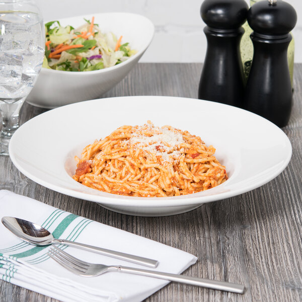 A bowl of pasta with cheese and a salad on a table.