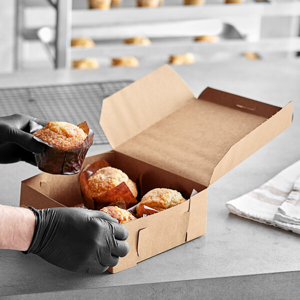 A person in gloves holding a brown muffin in a Kraft bakery box.