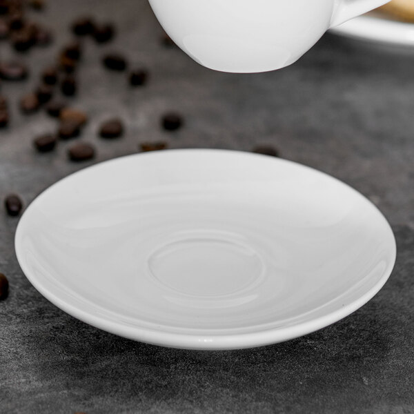 A white Tuxton saucer with a cup on a white surface.