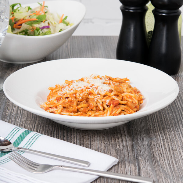 A bowl of pasta with cheese and a bowl of salad on a table with a Tuxton Modena AlumaTux Pearl White china bowl.