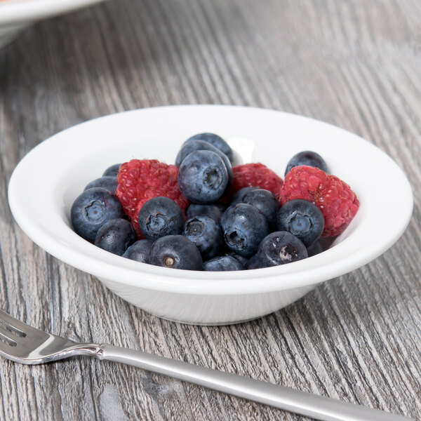 A Tuxton Modena AlumaTux white china bowl filled with blueberries and raspberries on a wood table.