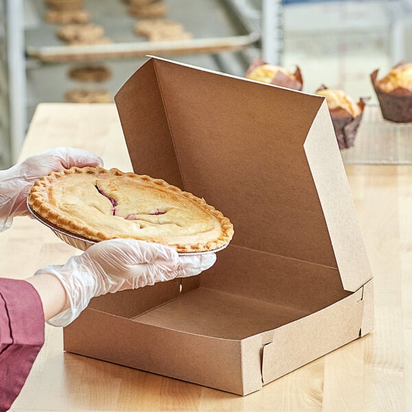 A person in gloves holding a pie in a 10" x 10" Kraft bakery box.
