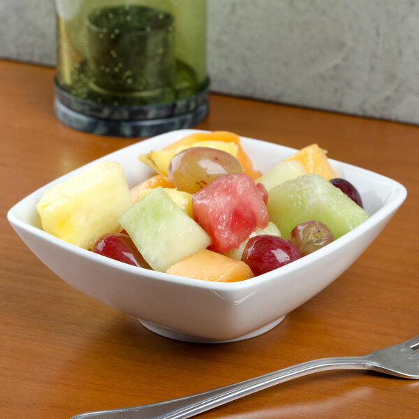 A bowl of fruit salad in a Tuxton bright white square china bowl on a table.