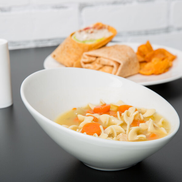A Tuxton TuxTrendz bright white china bowl filled with soup with noodles and carrots on a table.