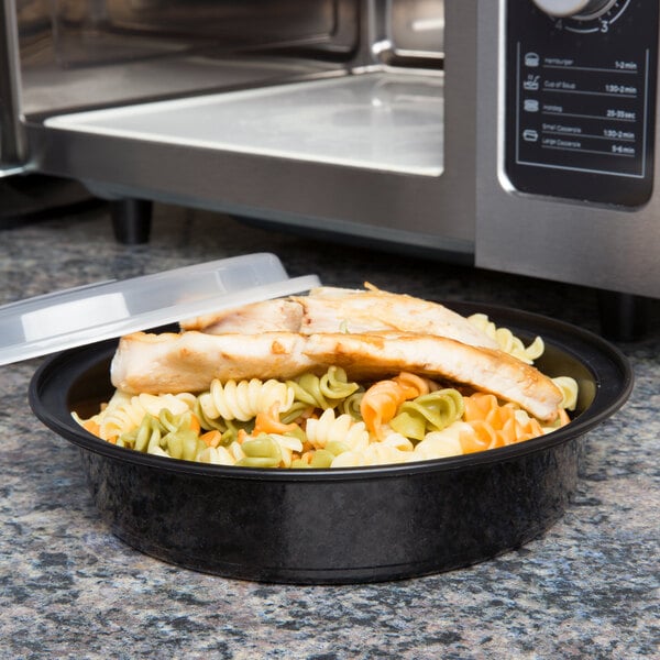 A close-up of a bowl of pasta with chicken and sauce in a Pactiv black plastic VERSAtainer.