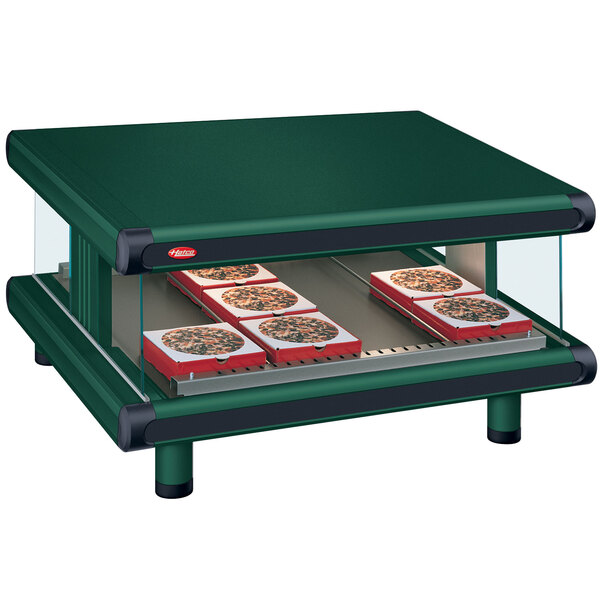 A Hatco countertop food warmer with pizzas displayed on a green shelf.