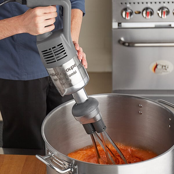A person using a Robot Coupe immersion blender to mix food in a pot.