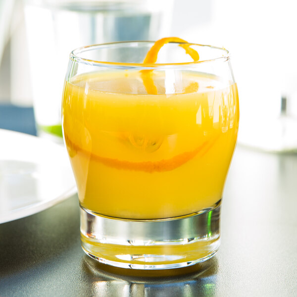 A Libbey rocks glass filled with orange juice on a table.