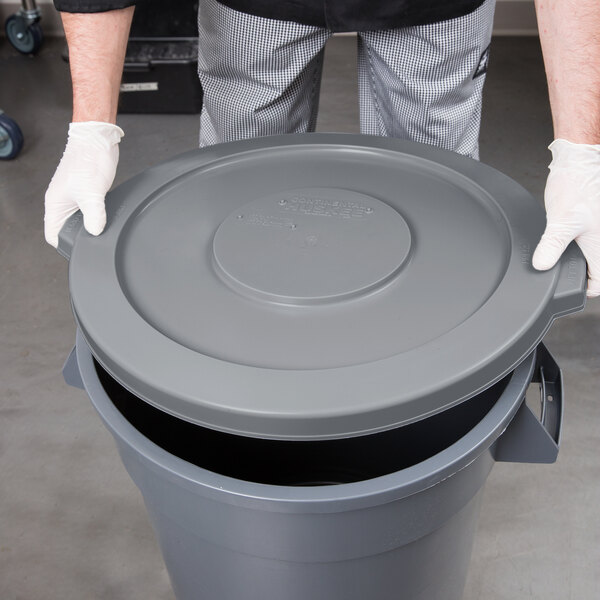 A person in a white shirt and gloves holding a Continental round grey trash can lid.