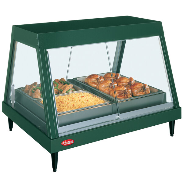 A Hatco stainless steel food warmer with a green glass display case containing food trays of chicken and rice.