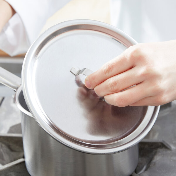 A person holding a silver lid over a pot on a stove.