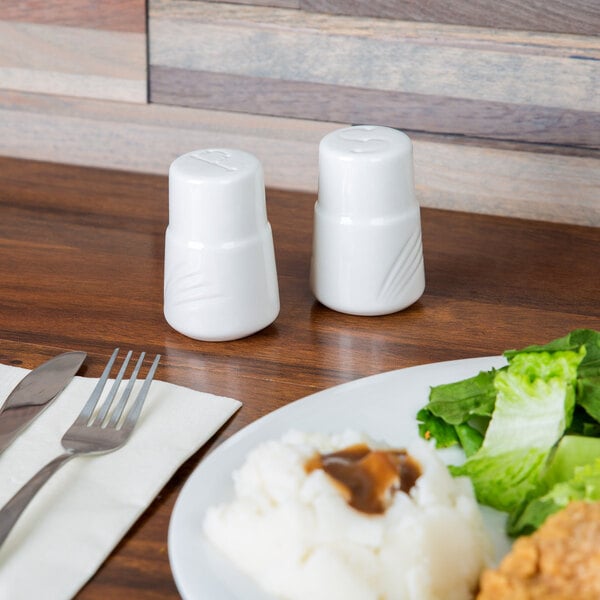 A plate of food with a CAC white porcelain pepper shaker on a table.