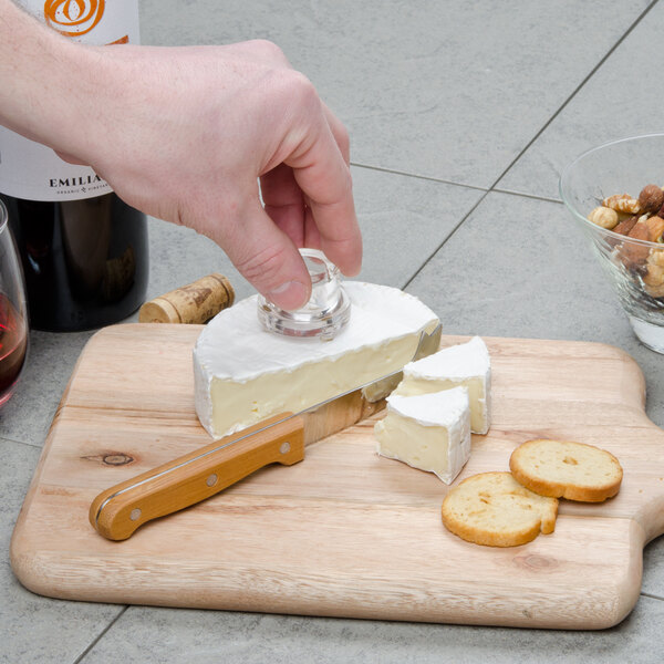 A person's hand using a Franmara cheese button clincher to cut cheese on a cutting board.