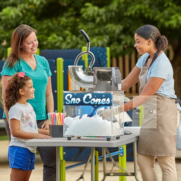 A woman and a girl at a Carnival King snow cone machine on a white table.