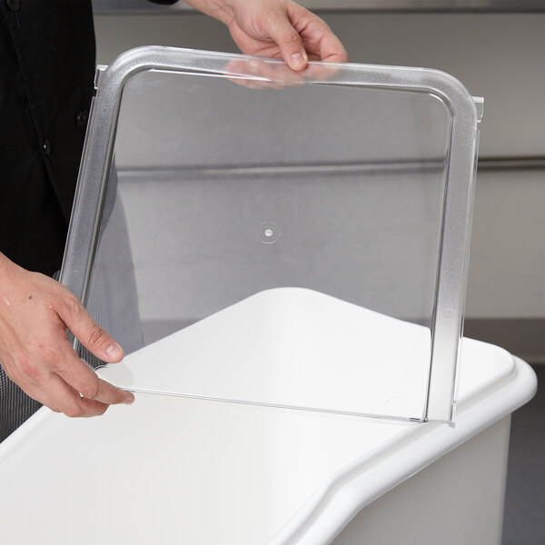 A person holding a clear plastic cover over a white Cambro IBS27 ingredient bin.