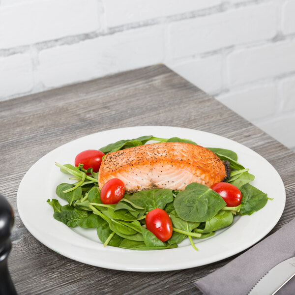 A Tuxton AlumaTux Pearl White china plate with a meal of salmon, spinach, and tomatoes on a table.